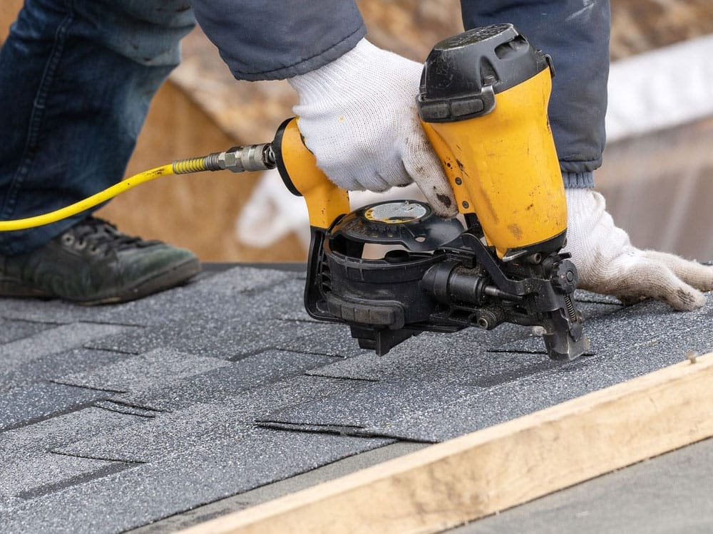 Roofing contractor using a nail gun to install asphalt shingles during a residential roof repair. Roof Dudes Midwest specializes in professional roof repairs, replacements, and storm damage restoration for both residential and commercial properties."