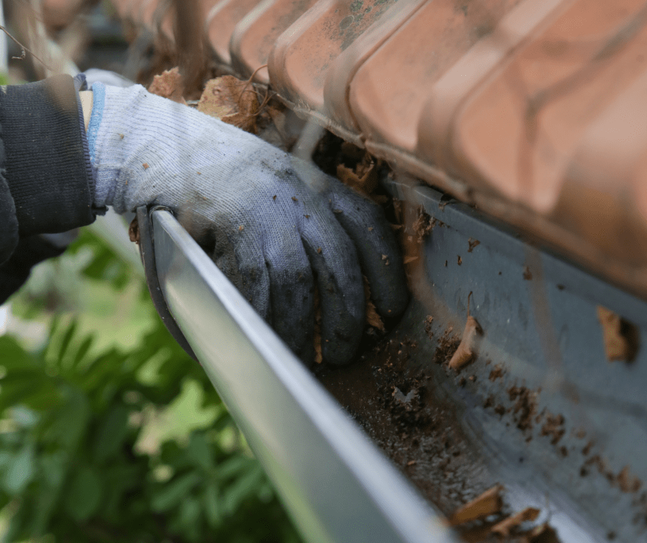 Clogged gutters can worsen small issues. A gloved hand clearing debris highlights the need for gutter cleaning and repair in Cincinnati.