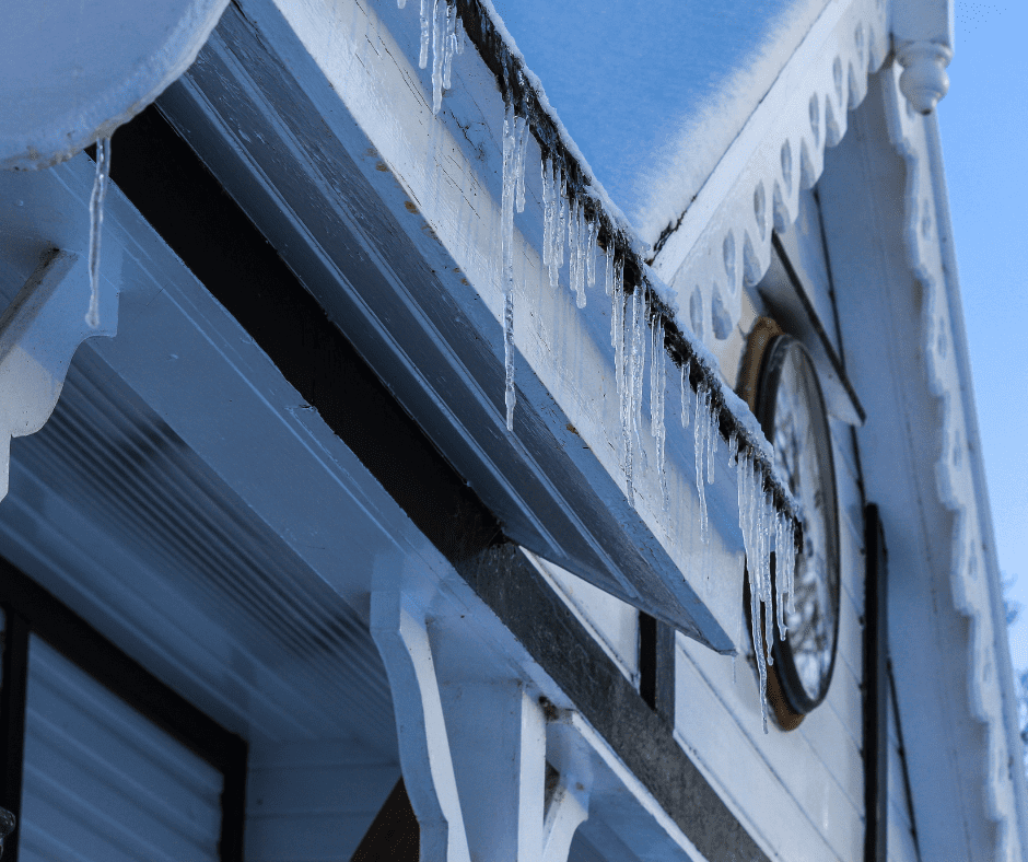 Icicles hang from a snow-covered roof edge. This shows the need for a roofer in West Chester. They can help with winter roofing issues like ice dams and snow buildup.