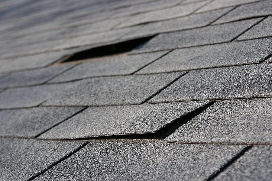 Close-up of a roof with missing and damaged asphalt shingles, exposing potential vulnerabilities that may lead to water leaks or other roofing issues.