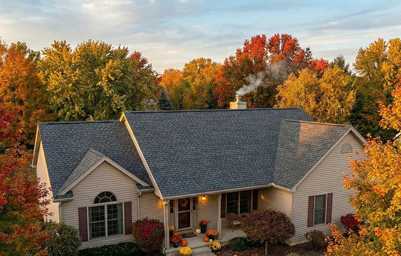 Home with a new roof surrounded by fall foliage, showing a completed fall roof replacement before winter.